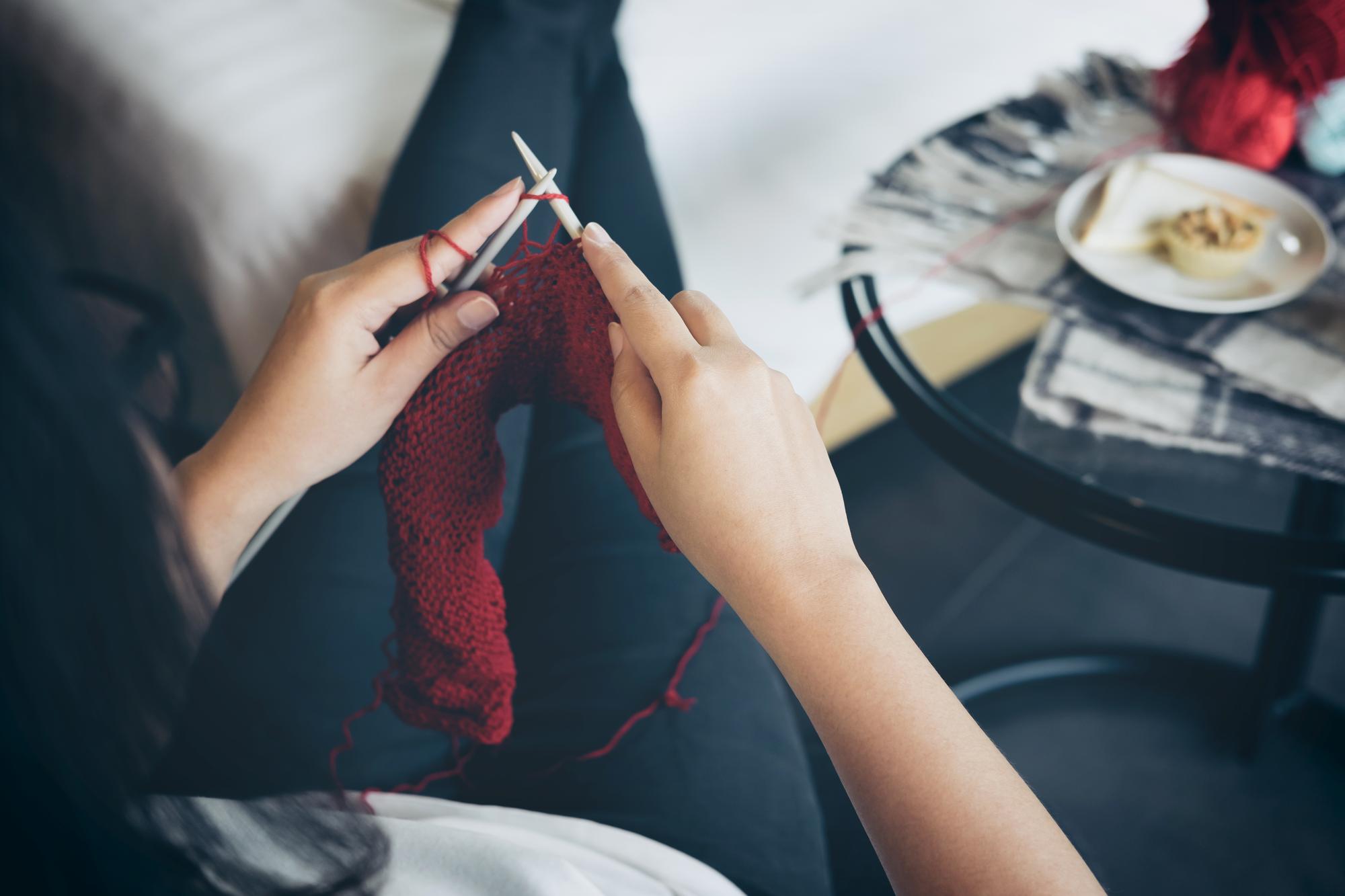 Hand mit Sticknadel über feinem Stoff im Atelier